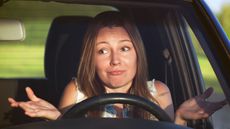 A driver shrugs while sitting behind the steering wheel of her car.