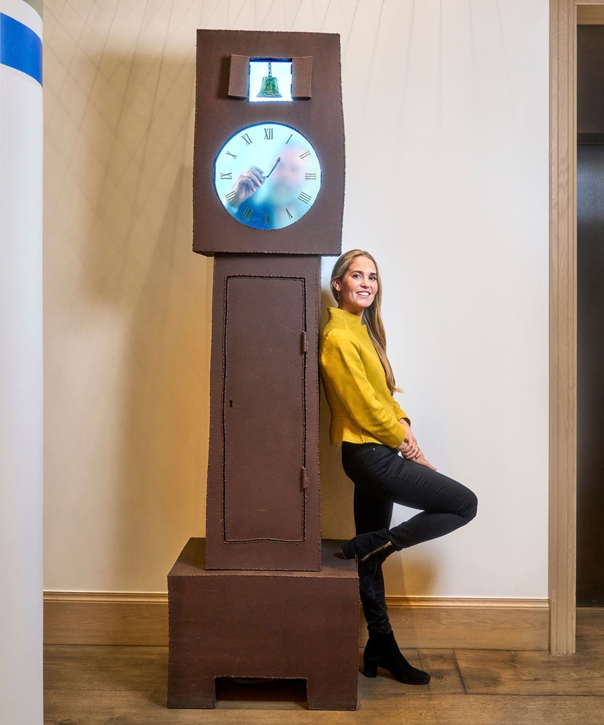 Designer Willow Kemp leaning against a piece of artwork that looks like a grandfather clock