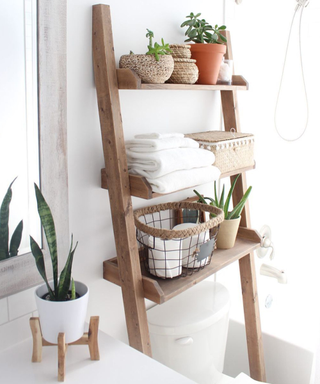 Rustic over-toilet shelf ladder styled with towels, plants and woven storage baskets