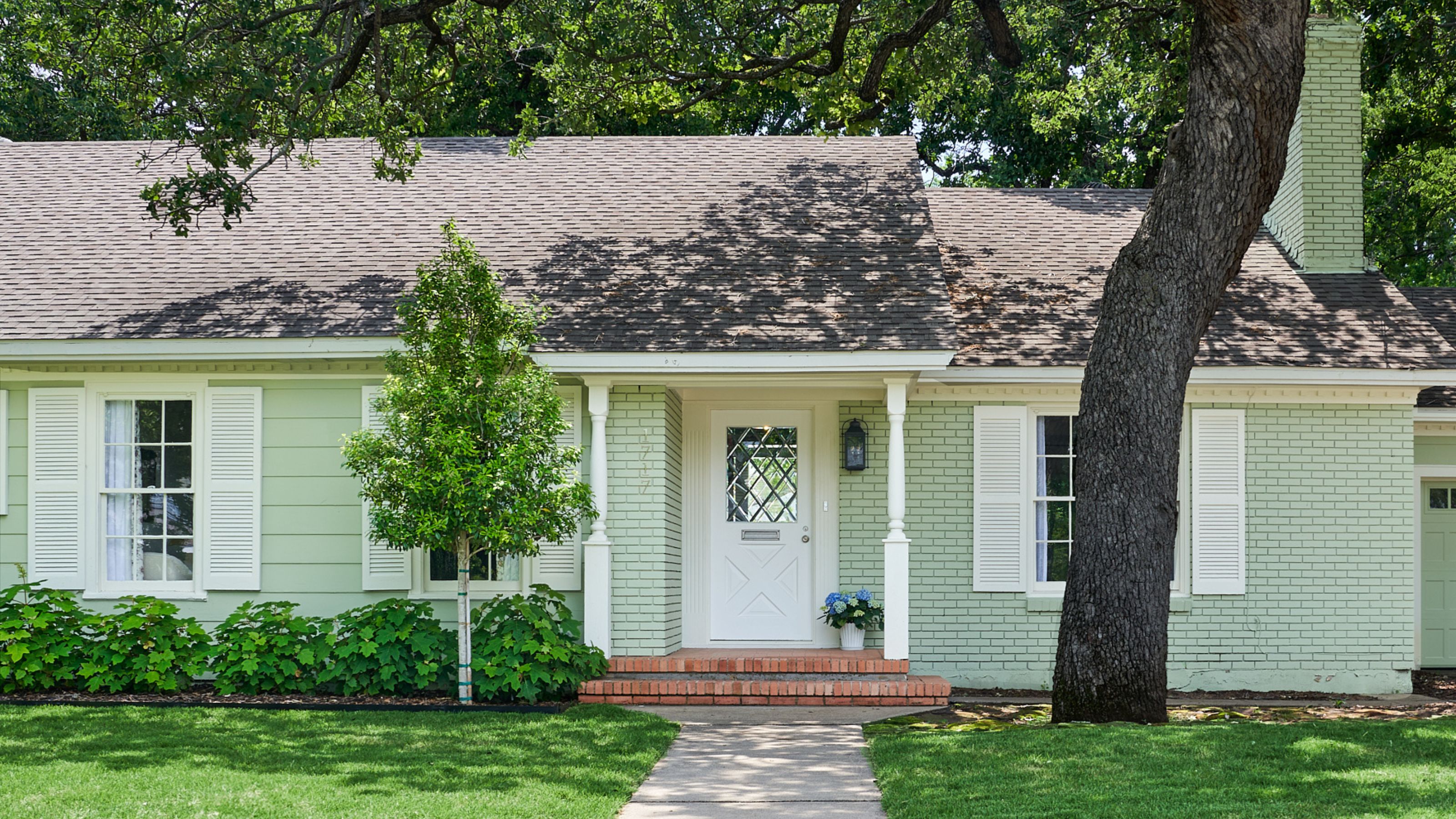 a pale green painted brick home with low roof, chimney, white front door and porch