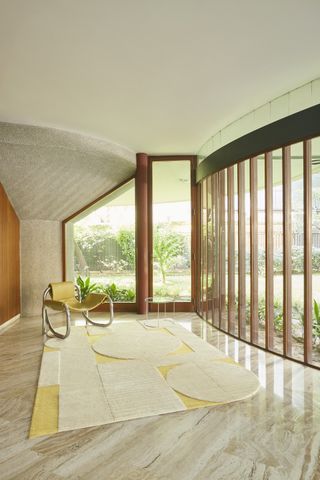 A white and yellow rug, featuring a repeating circular motif, photographed inside a modernist house next to a large window and yellow armchair