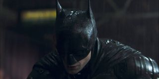 Batman (Robert Pattinson) stands over a thug in the rain in The Batman (2022)