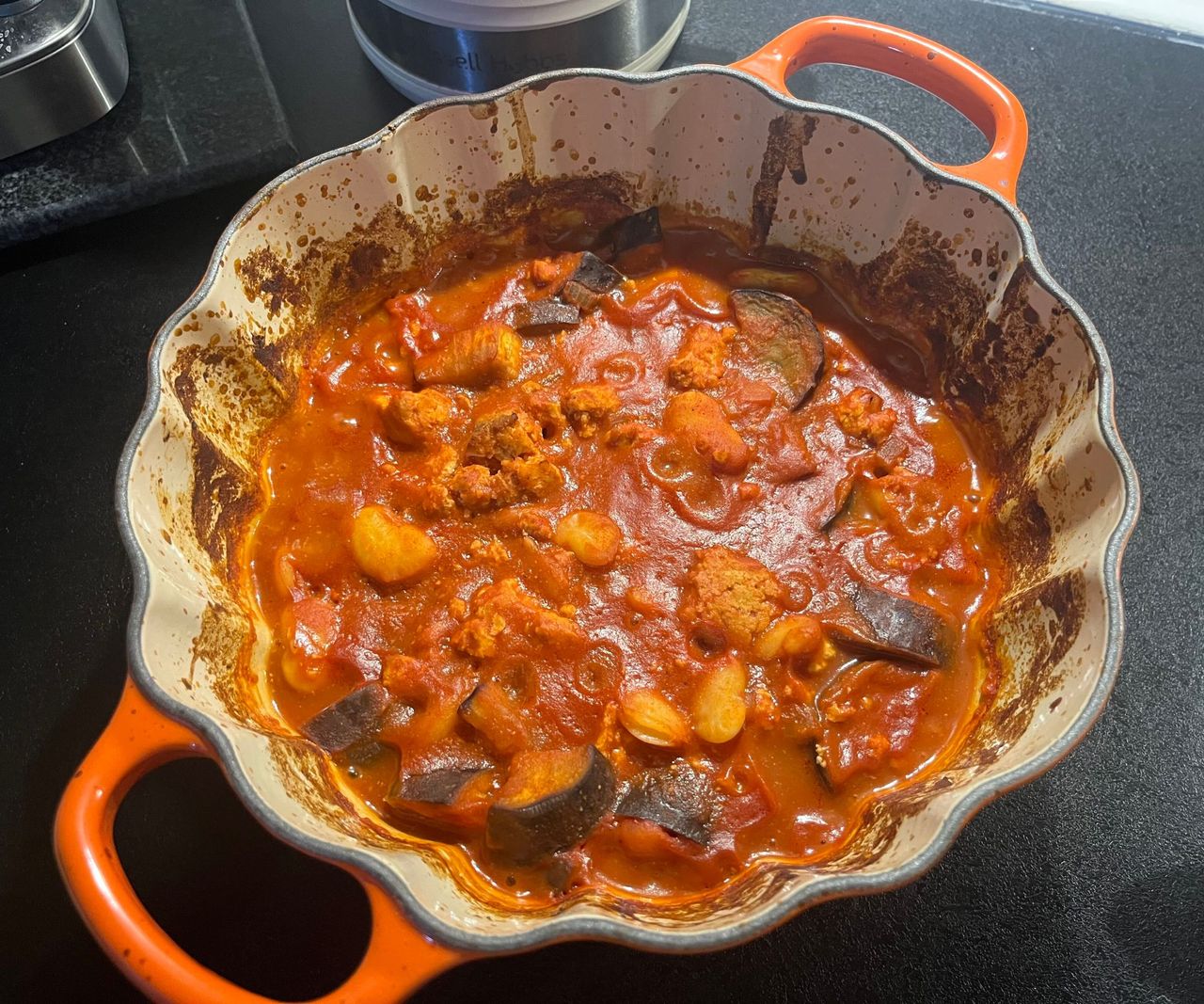 An orange Le Creuset Pumpkin cocotte on a black counter filled with a tomato and bean stew.
