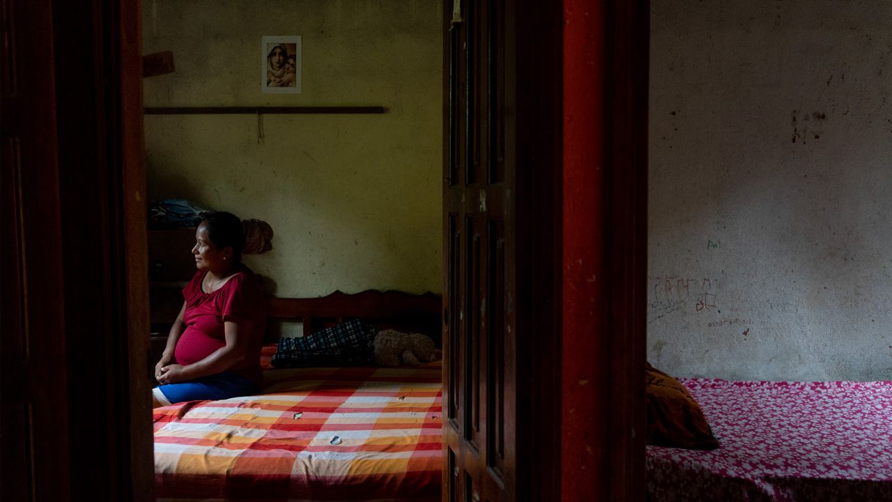 Woman sat on bed in dark room.