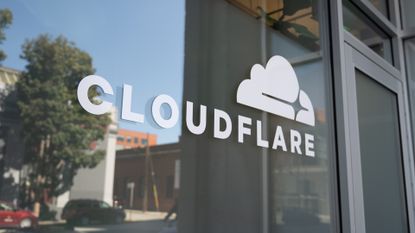 Cloudflare logo and branding pictured on a glass entryway in San Francisco, California, with street reflected on glass.