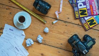 A flatlay of a camera and lens, two tape measures and some notes depicting the concept of focal length 