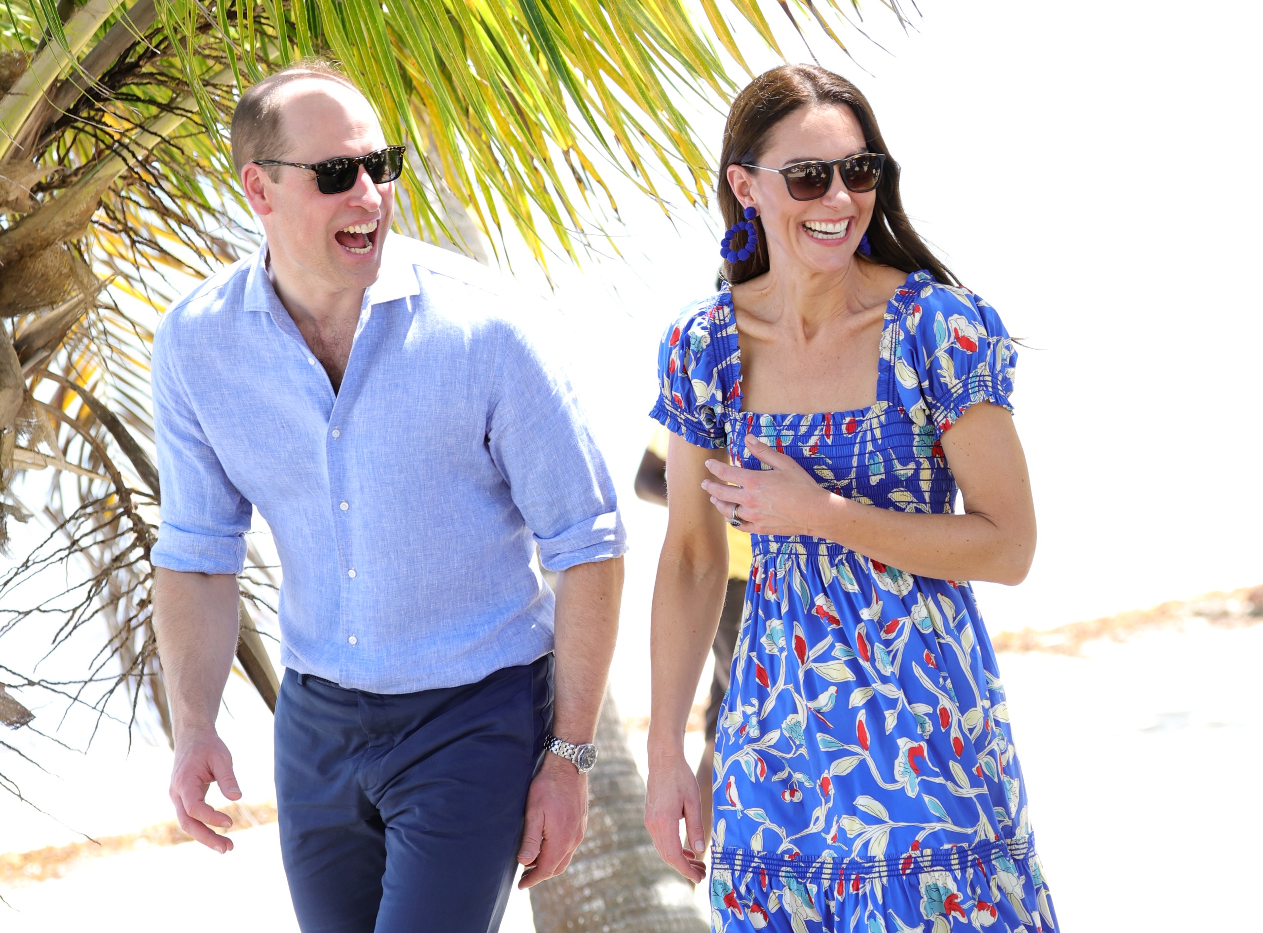Prince William and Princess Kate wearing sunglasses and laughing in front of a palm tree