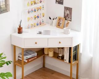 A white corner desk with art on the wall and supplies on the desk