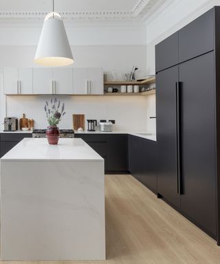 A black and white kitchen with a white kitchen island, black cabinets and fridge, white countertops with chopping boards and appliances, and white wall cabinets