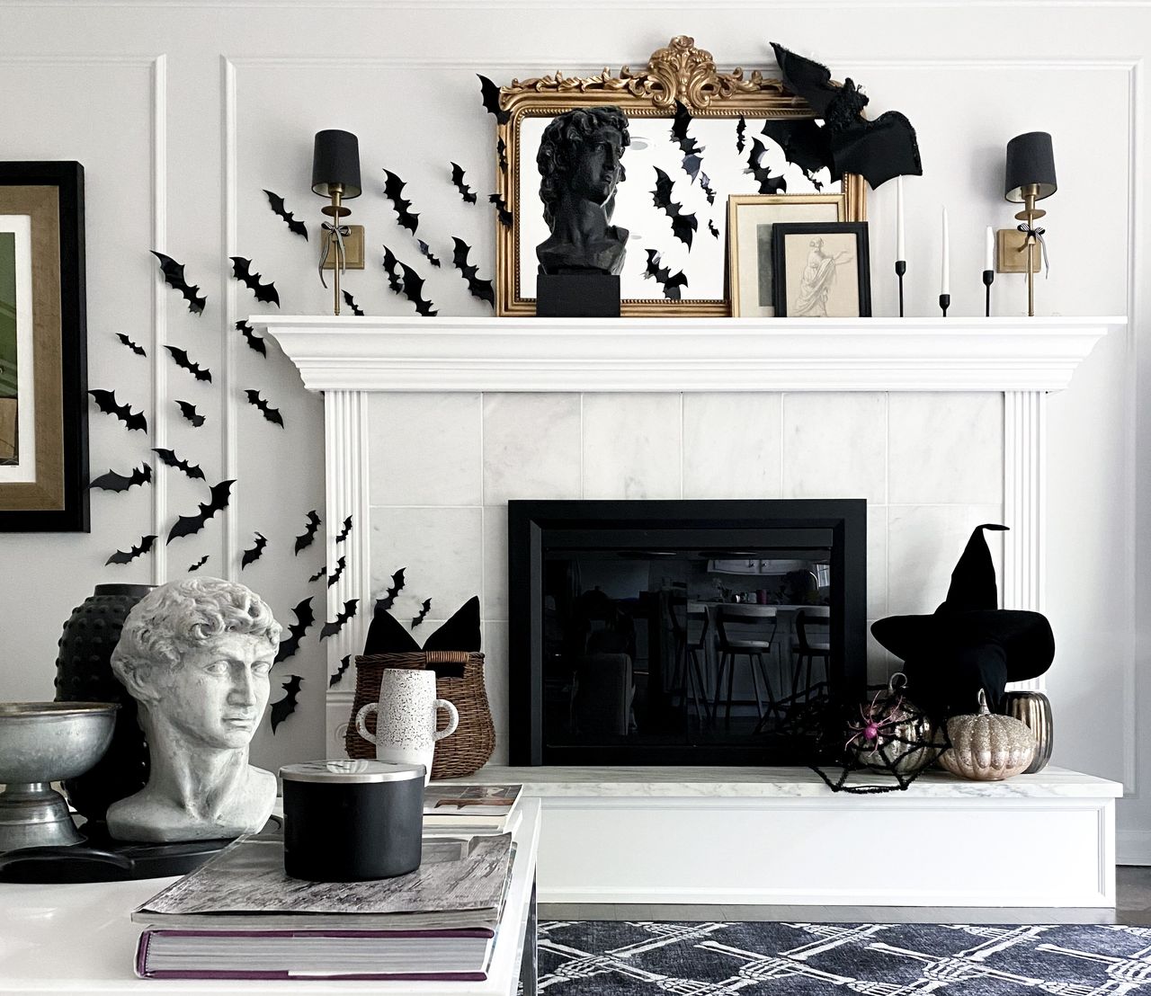 A living room with a white fireplace decorated with Halloween decor including a witch&#039;s hat, bats, and candles in tapers