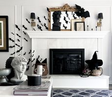 A living room with a white fireplace decorated with Halloween decor including a witch's hat, bats, and candles in tapers