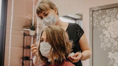 woman getting hair cut, both wearing face masks