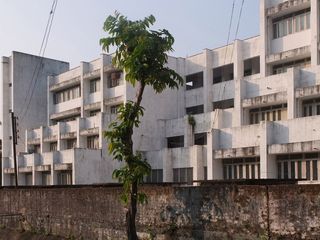 The exterior of the Chittagong University. White facade, that's been weathered by natural elements. The lowest part of the building is the longest, while each floor above it is pulled in.