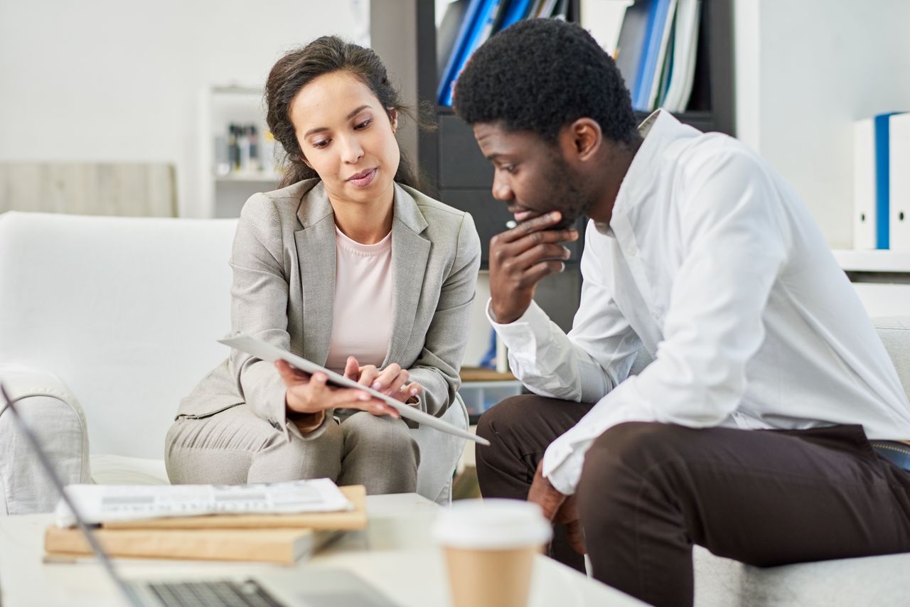 Woman showing documents to man while sat on sofas