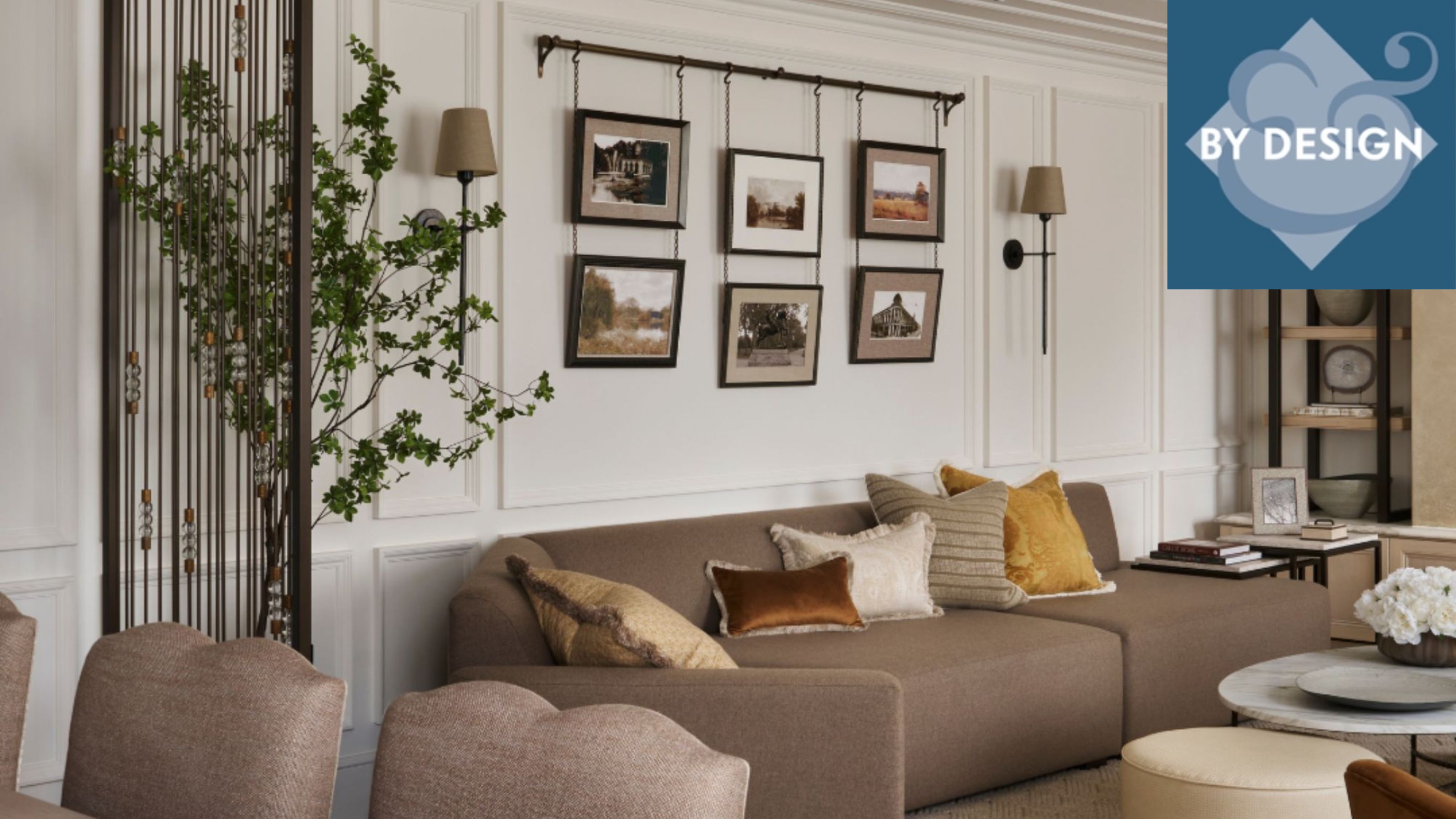 Neutral, cozy living room with brown sofa and scatter pillows, coffee table and ottoman in front gallery wall and lights on wall above, greenery, shelves in the background, dining chairs in foreground