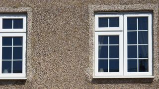 A pebbledash facade on a house with two PVC windows