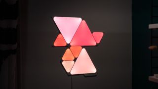 Ett par Nanoleaf Shapes sitter på en vägg och lyser i olika rosa och orange nyanser.