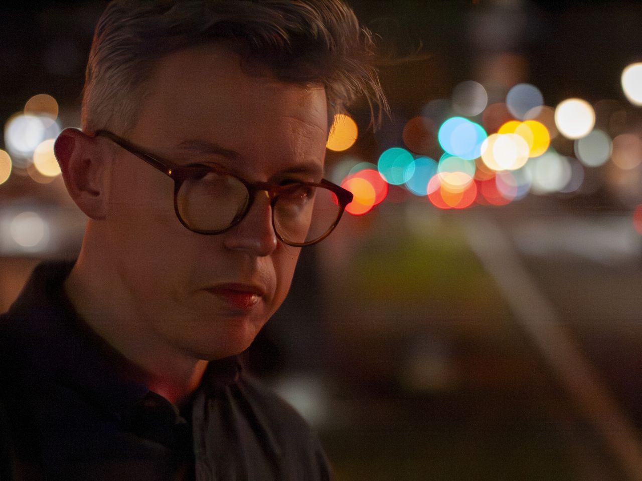 Portrait of a man at night in a city, there are blurred circular light behind him, shot with the Panasonic Lumix G1