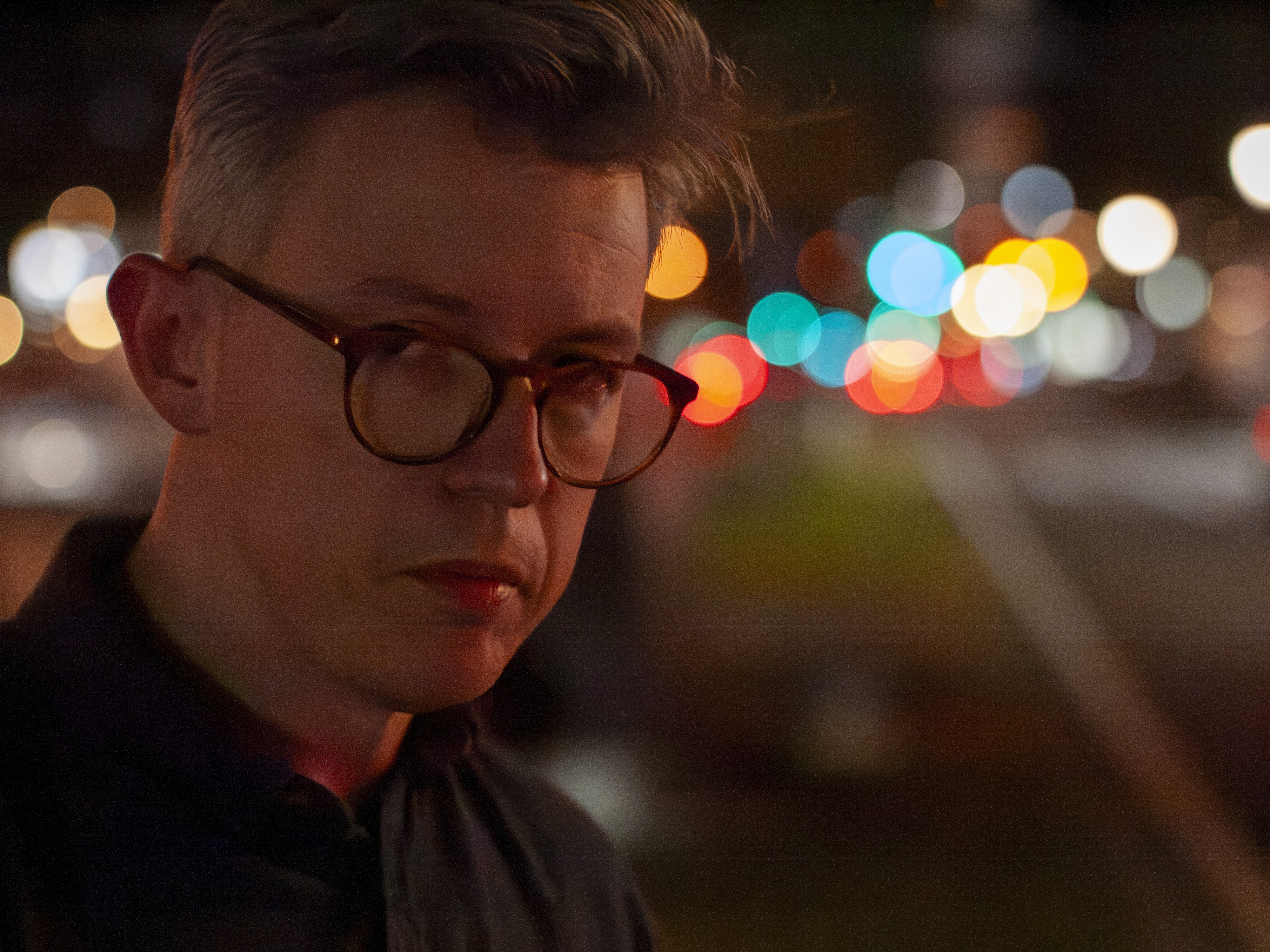 Portrait of a man at night in a city, there are blurred circular light behind him, shot with the Panasonic Lumix G1