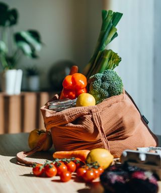 A brown bag with orange, yellow, and green vegetables around it on top of a wooden countertop