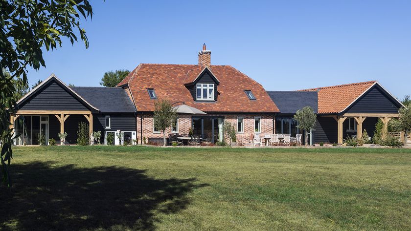 An angled view of a barn conversion with extensions clad in black timber out either side