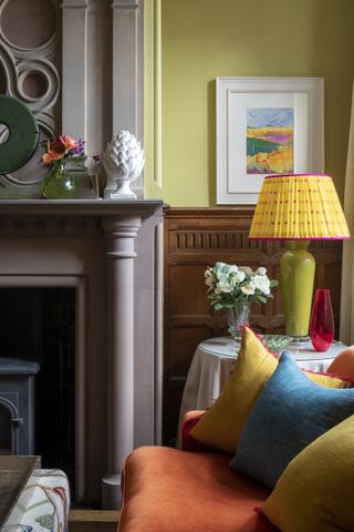 living room corner with bright table lamp, corner of orange sofa, yellow and blue cushions, yellow walls, fire surround