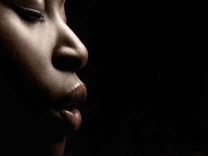 Cropped photo of a Black woman's face looking right against at black background