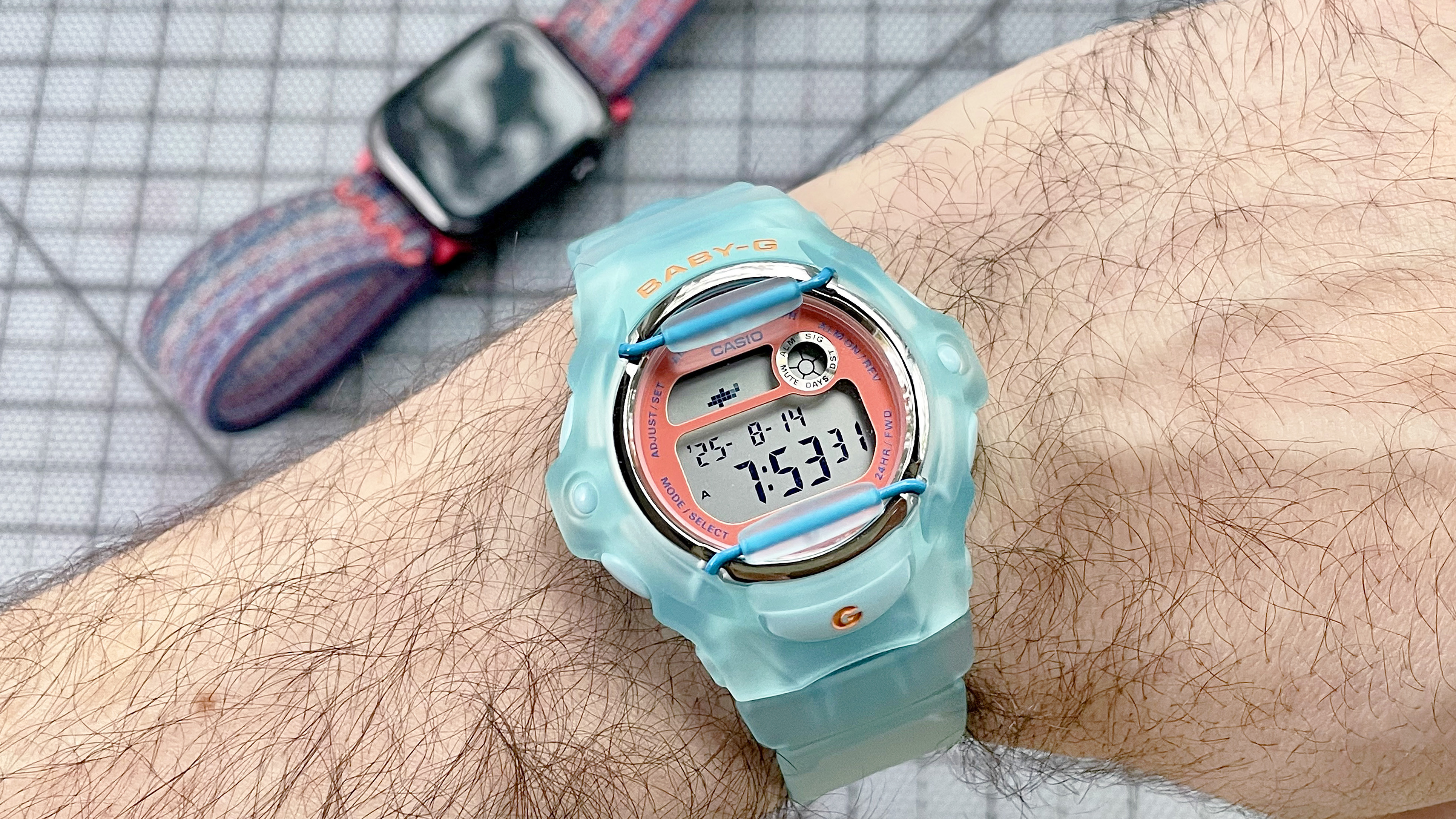 Close-up of the Casio Baby-G BG169 is semitransparent baby blue on the writer&#039;s wrist with an Apple Watch 10 out of focus in the background