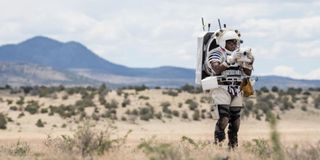 An astronaut in the desert wearing a space suit and using the Nikon Handheld Universal Lunar Camera (HULC)