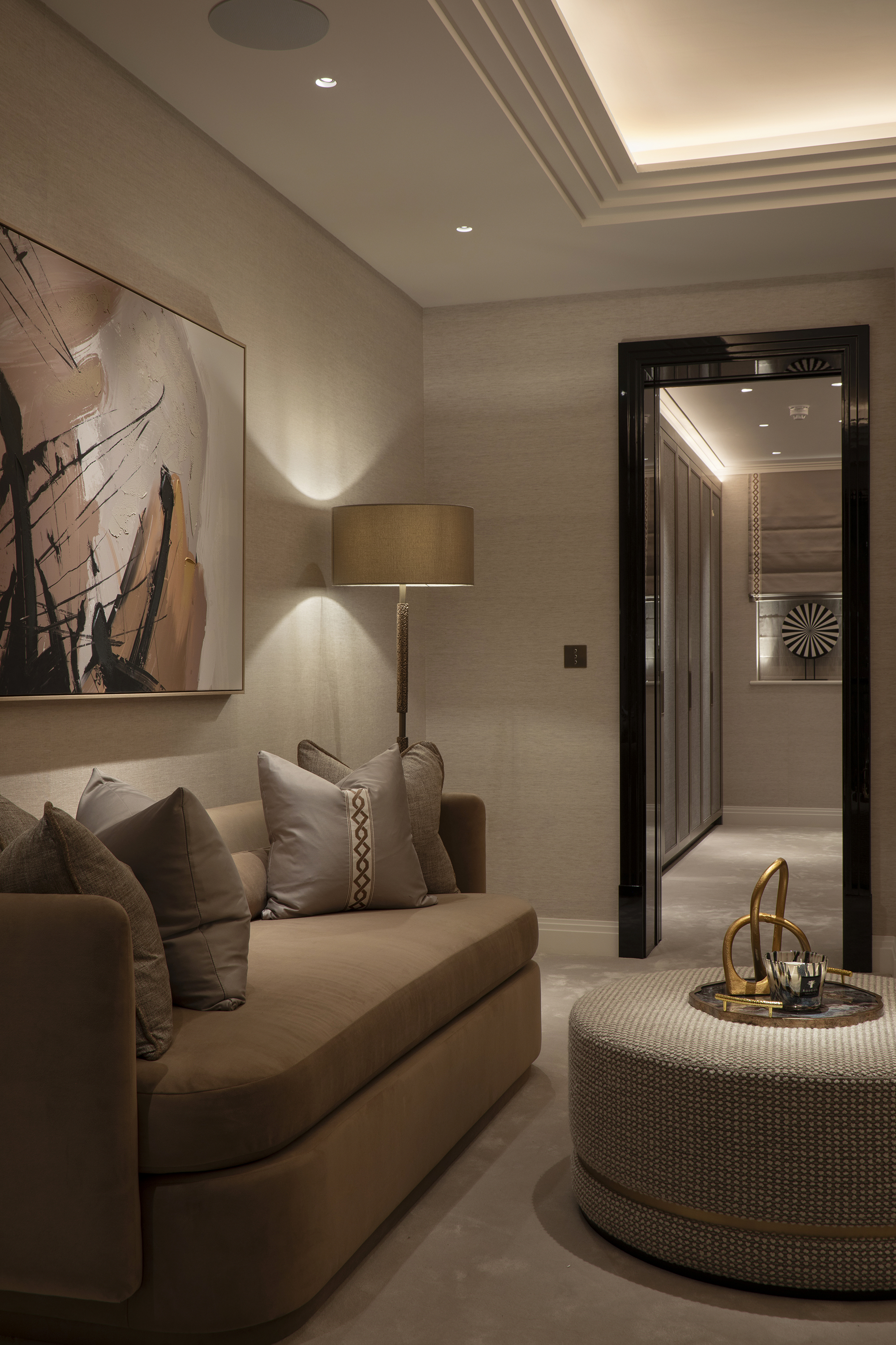 A living room with a seating area lit but spotlights, with abstract artwork on the walls and a floorlamp in the corner