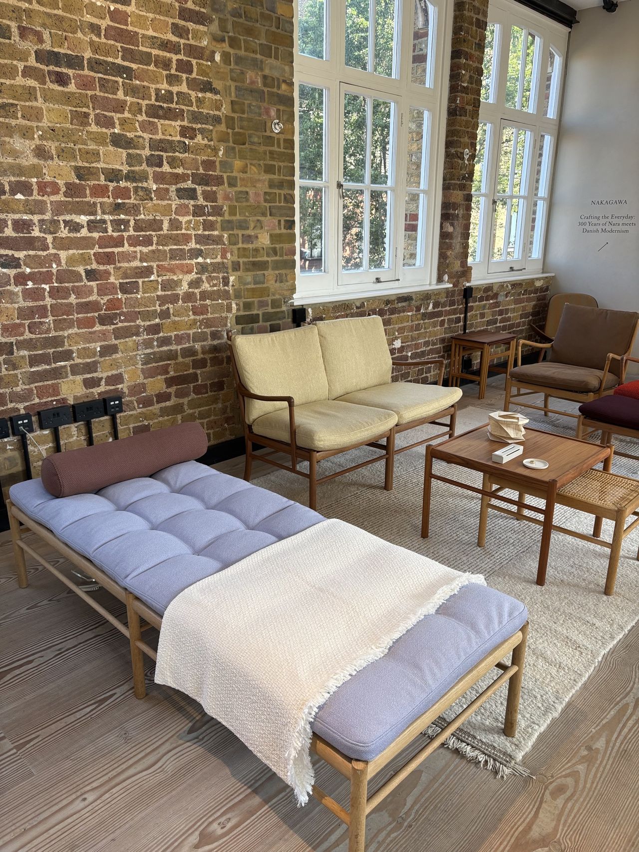 Image of a daybed in a brick room with a light blue cushion and a brown pillow. There are a few other wooden chairs and tables in the room.