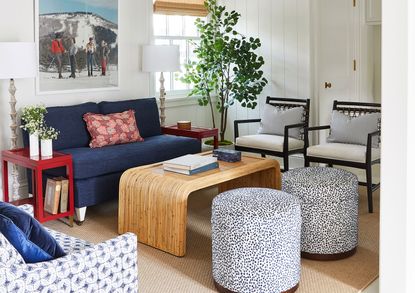 living room with white walls and blue sofa red cushion and wooden coffee table red side table and monchrome patterned upholstered stools