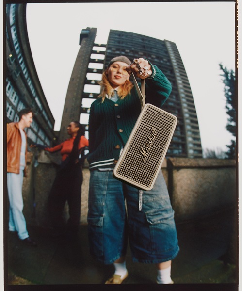 The Marshall Middleton II portable speaker in a model's hand by its strap in a cream color.