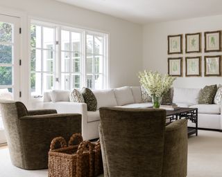 Living room with white walls and neutral carpet, L-shaped sectional and two brown armchairs
