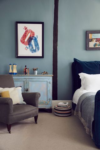 blue bed and blue walls with timber beam and graphic artwork and armchair