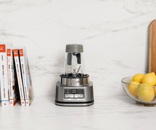 The Ninja Foodi Smoothie Bowl Maker on a marble countertop with a bowl of lemons on one side and some cooking books on the other