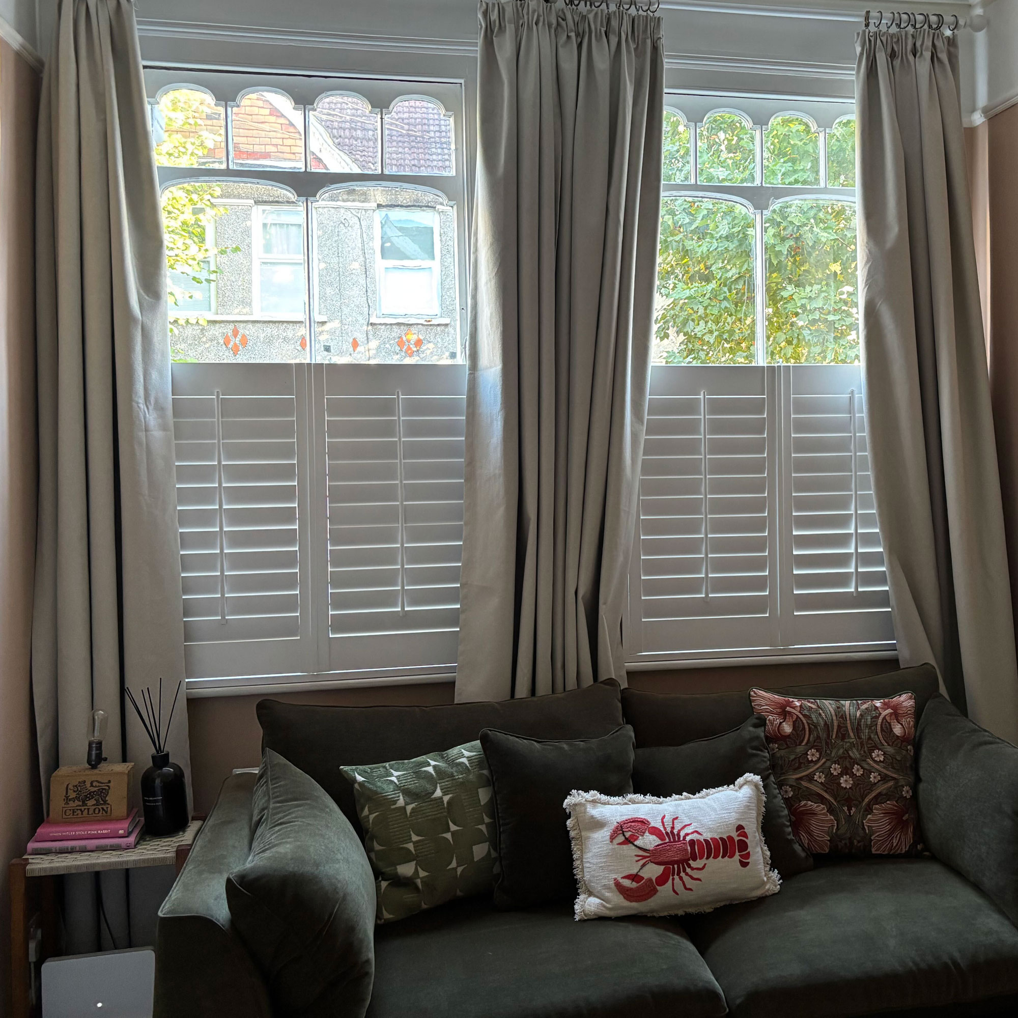 Curtains behind a green sofa with three cushions on it 