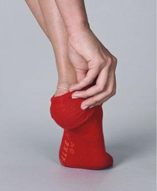Photograph of a woman pulling on a red sock.