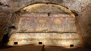 A mosaic covers the wall of a banquet hall, shaped to imitate a cave, in Roman remains.