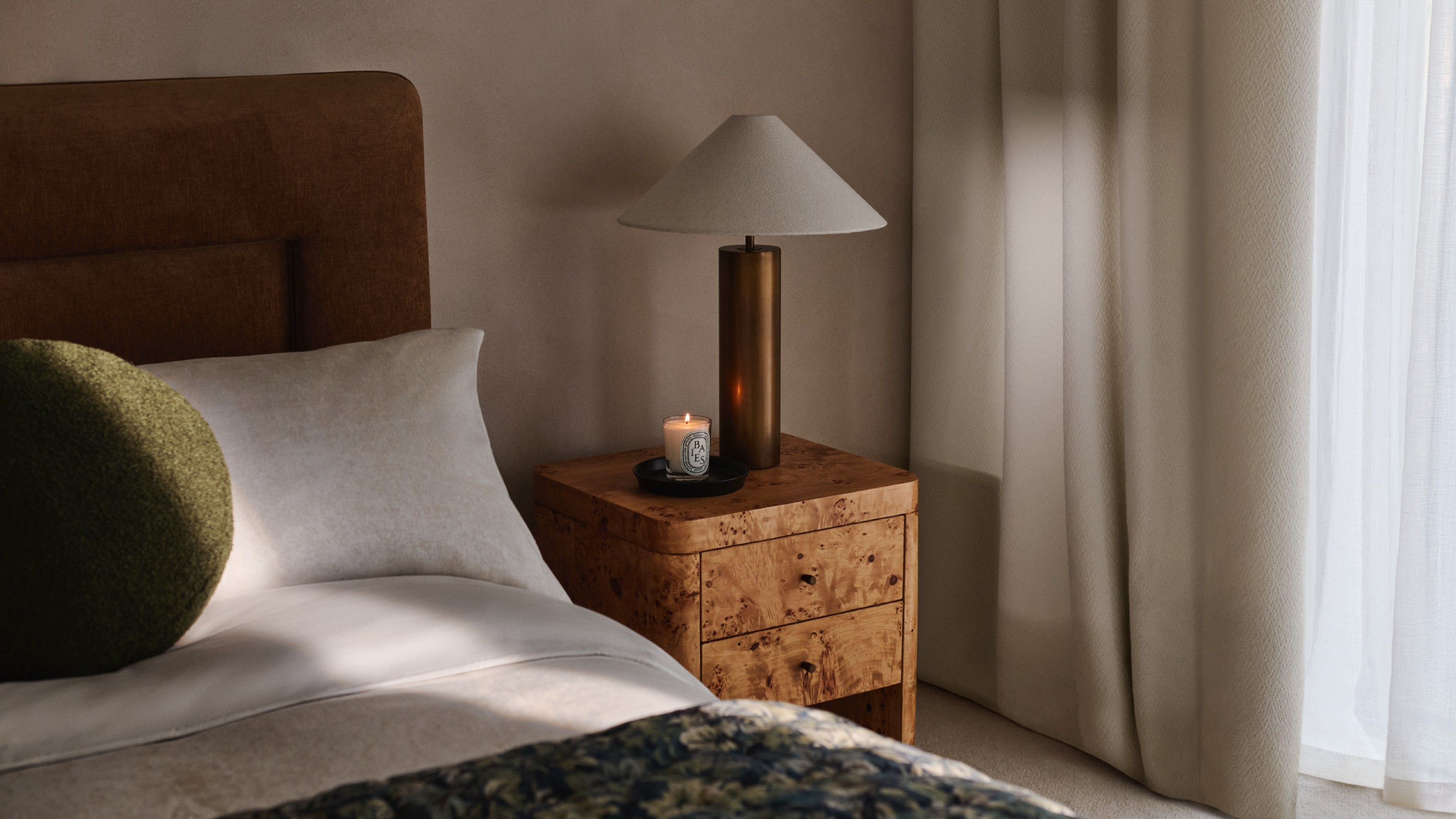 John Lewis Burl 2 Drawer Bedside Table in a bedroom with a table lamp on top and a lit candle