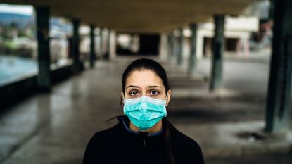 Masked unemployed woman looks up at camera