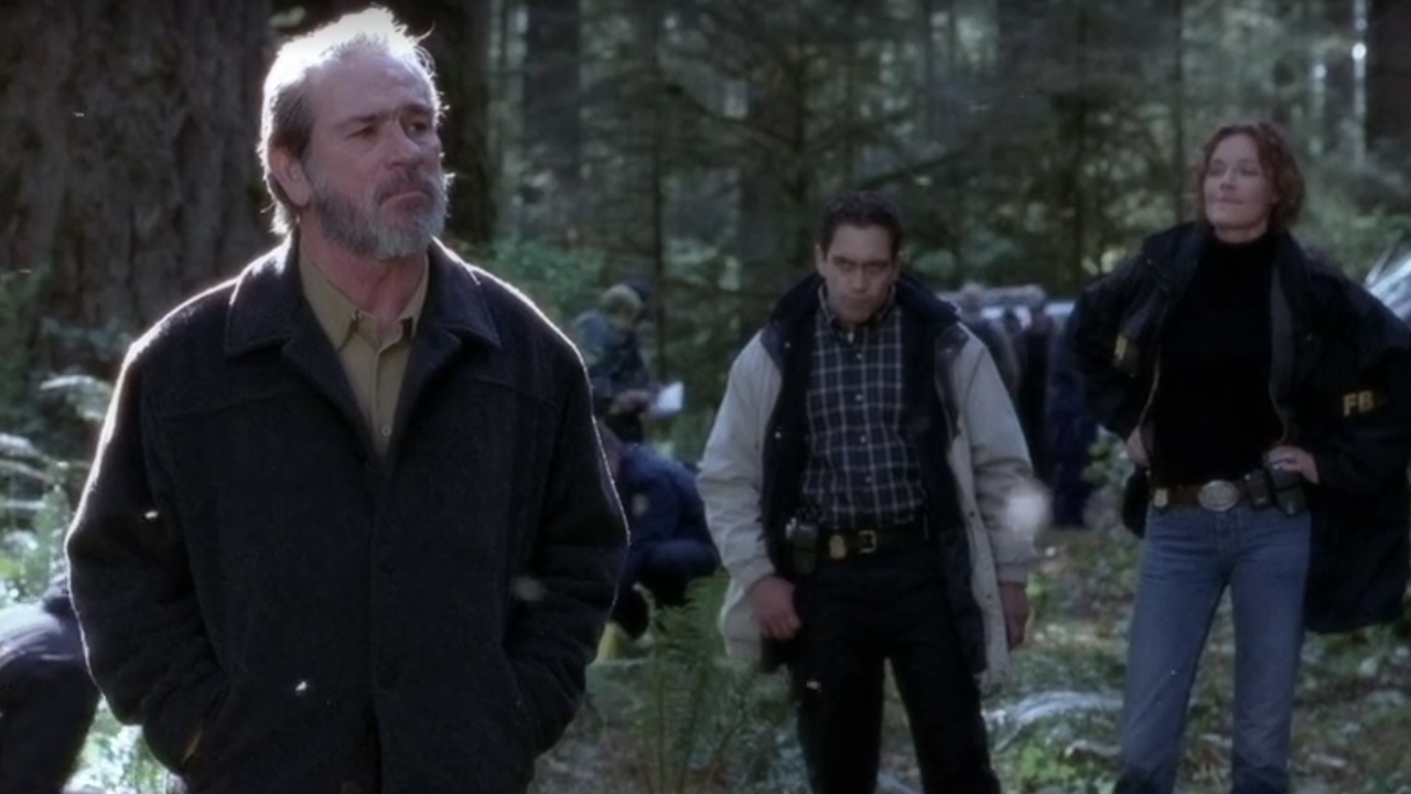 森の中の前景にトミー・リー・ジョーンズがおり、コニー・ニールセンとジョゼアキュートの前に立っています。 『ザ・ハンテッド』のザ・イガ