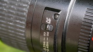 A close-up of a macro lens showing the focus switch is set to manual