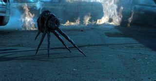 an insect-like alien on a street in front of burning cars