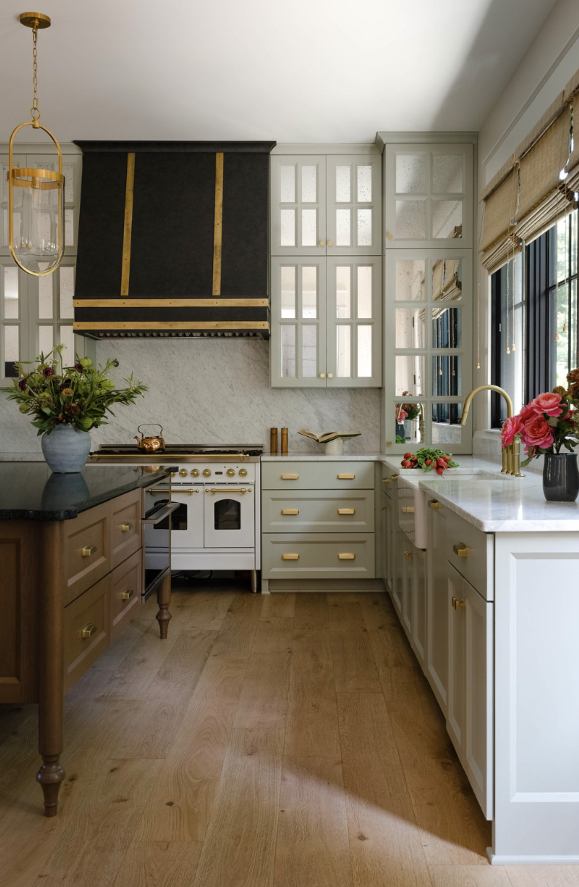 A kitchen with shaker cabinetry, wooden flooring, and a black range oven hood with gold trim