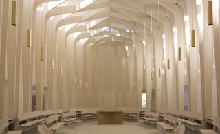 View of the main chapel looking towards the alter. A round area with benches and long round hanging pendant lights.