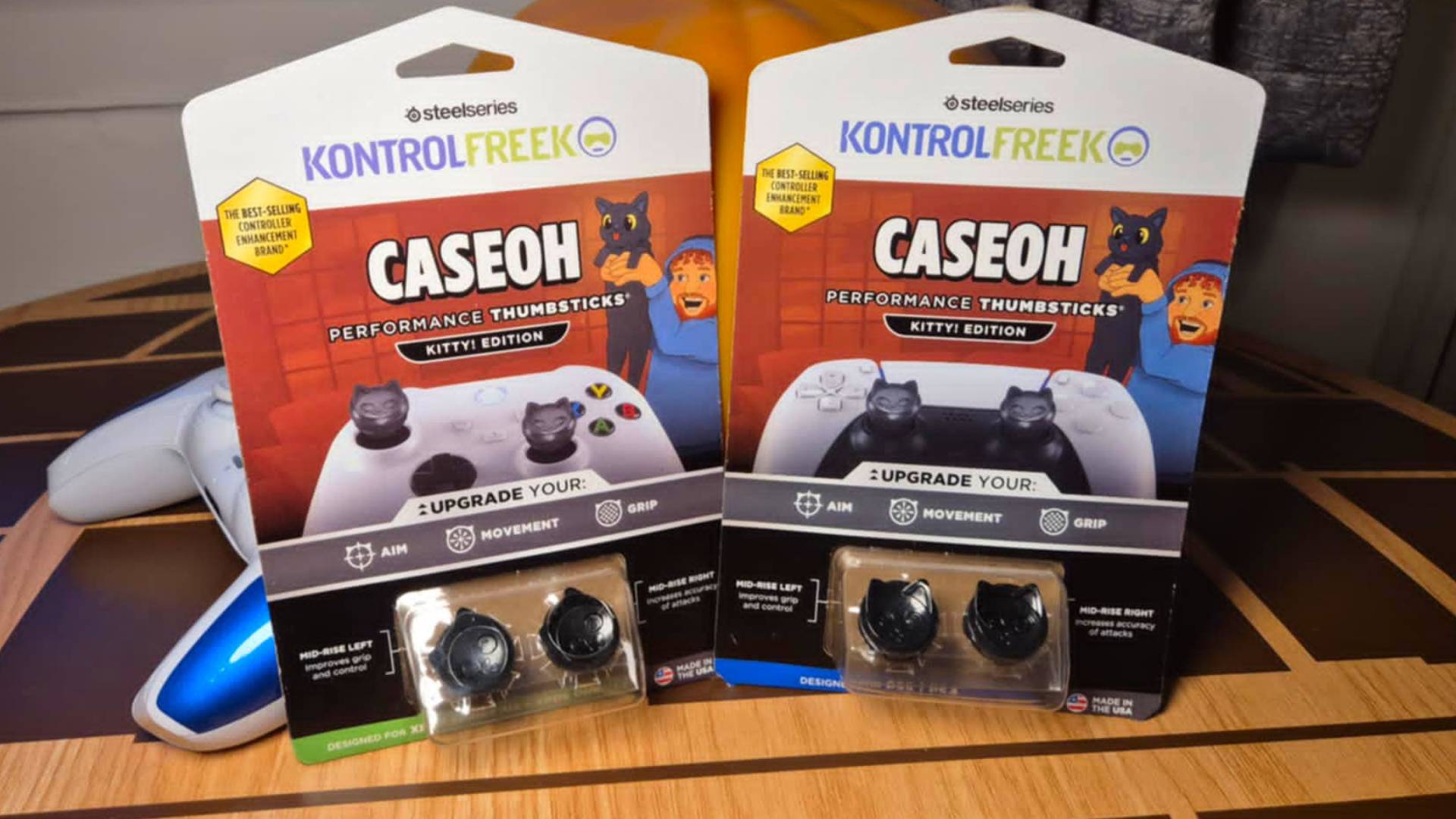 Photo of a pack of two thumbsticks sitting on a wooden table. The thumbsticks are black and look like the face of a cat.