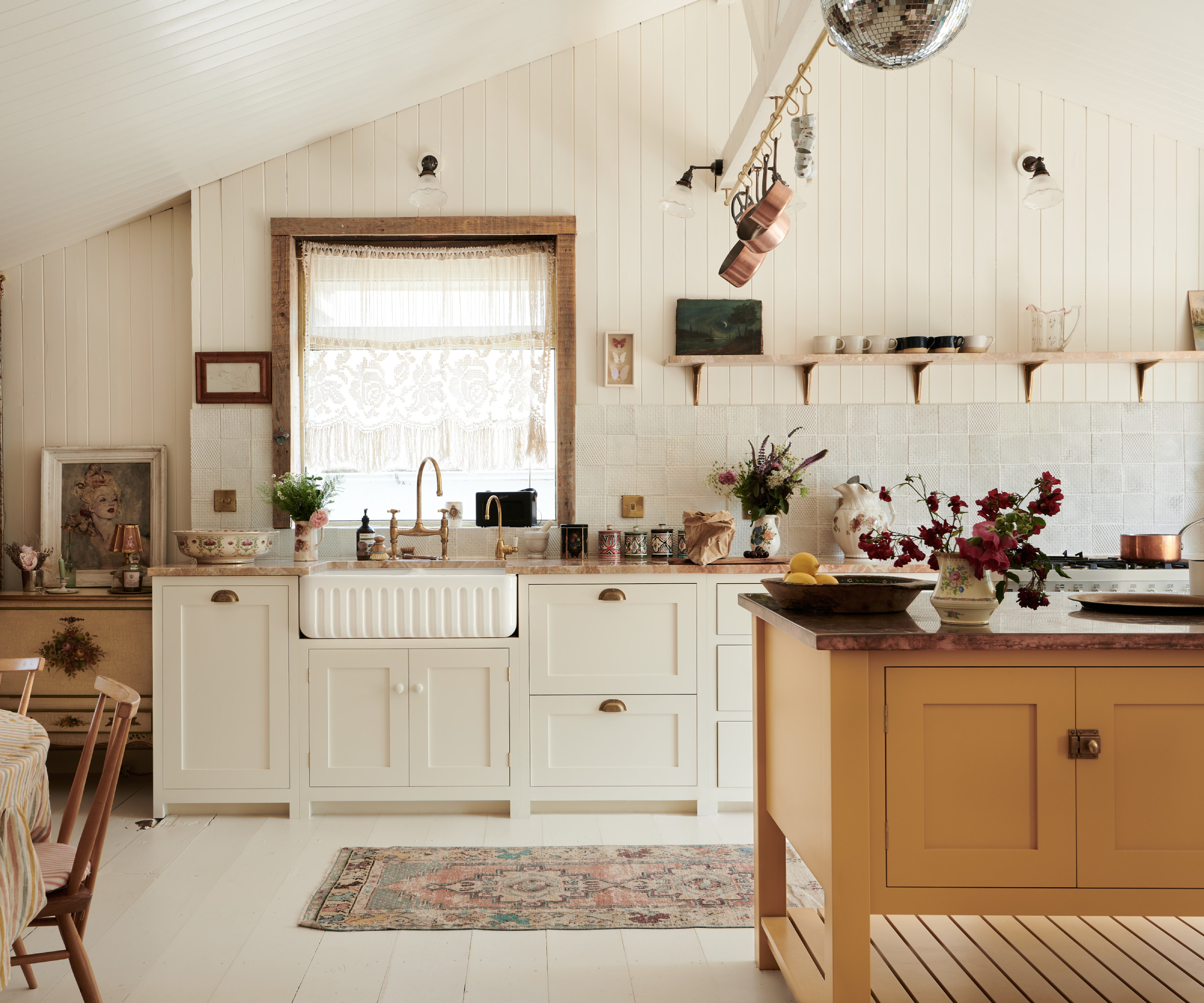 kitchen with white shaker units, window, yellow kitchen island, hanging copper pots, mirrorball, rugs on floor and rustic boho feel