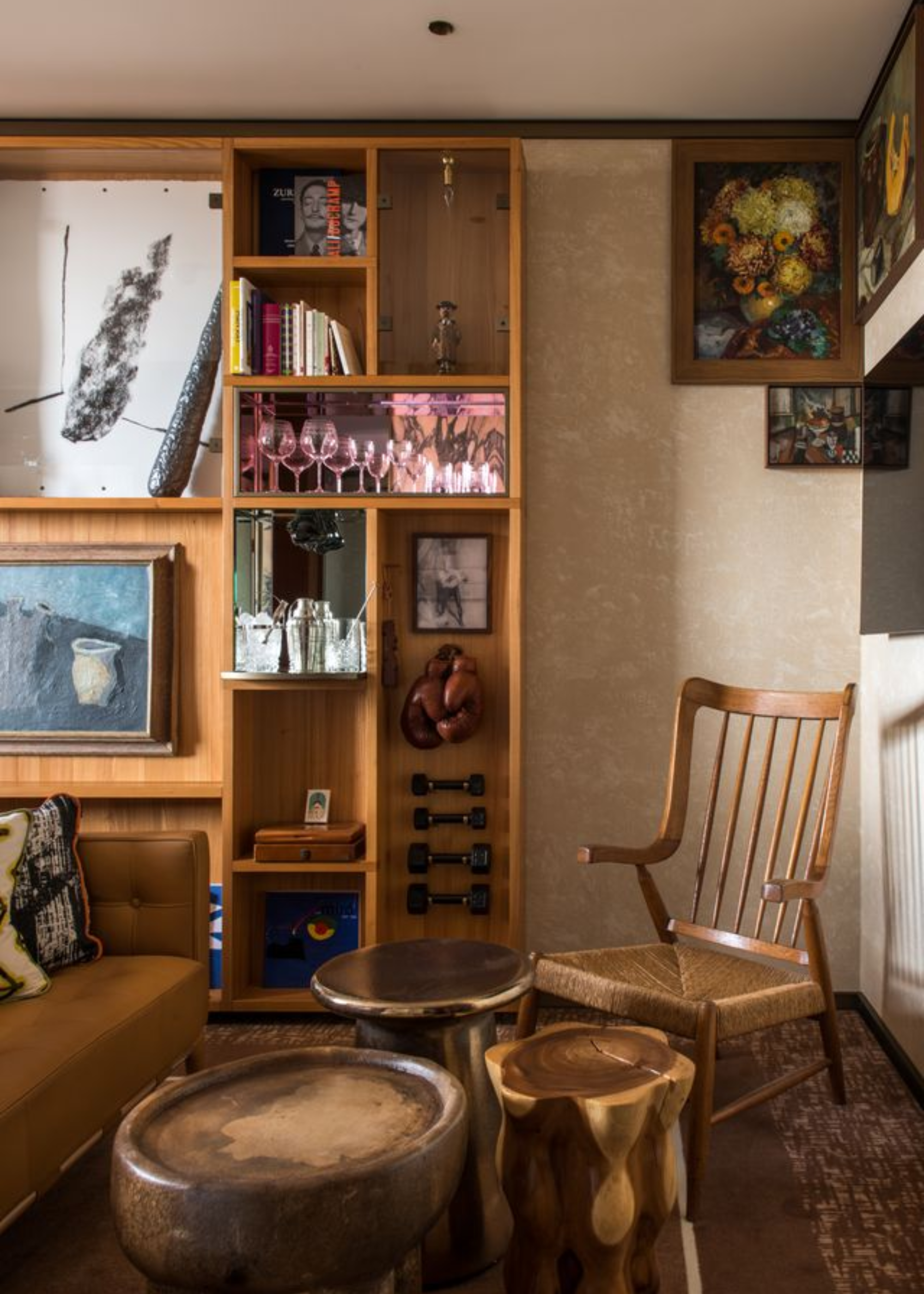 A corner of a hotel room with a chair, a trio of side tables, framed art, a mini bar and gym equipment