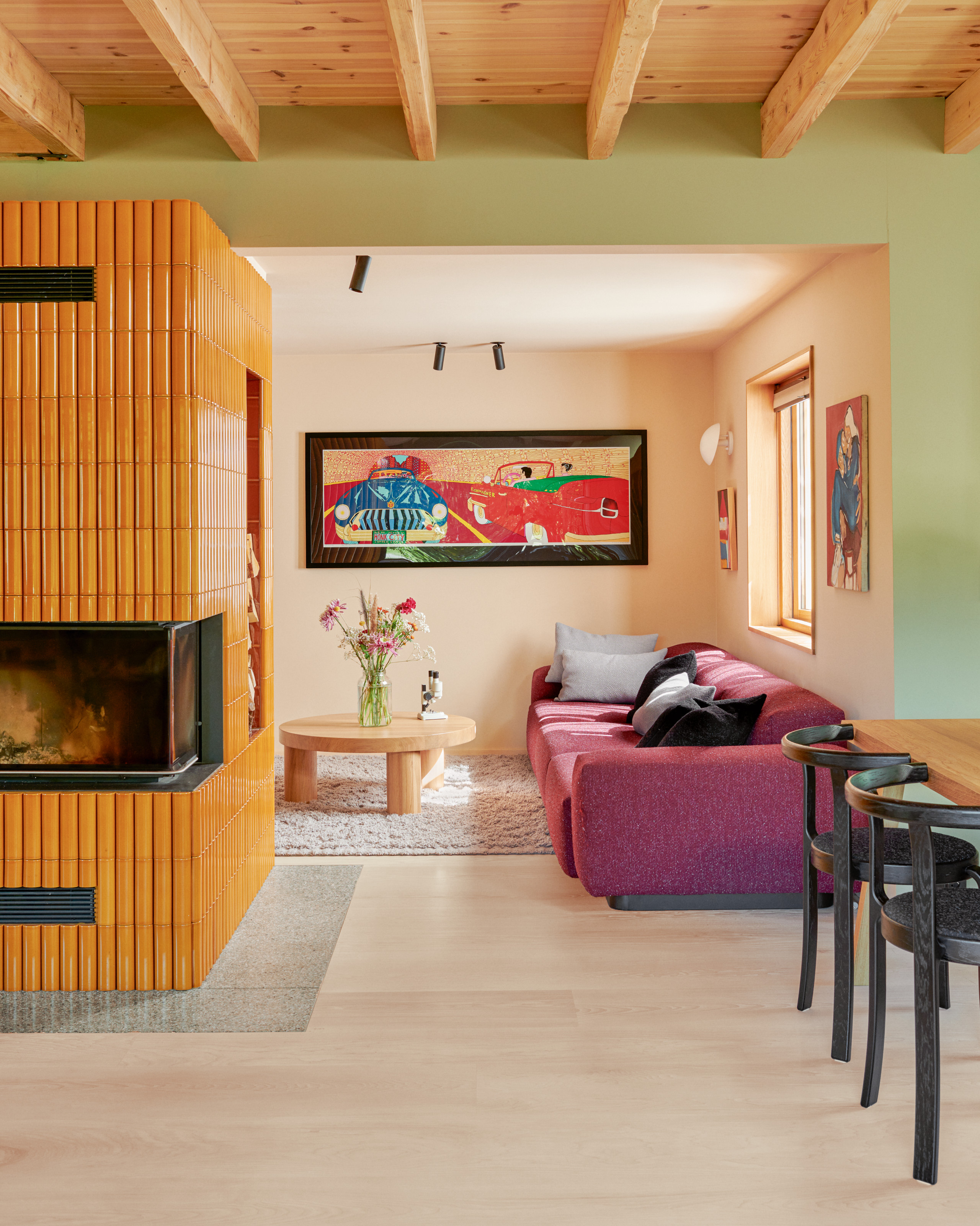 Living area of an open plan space with pale green walls, corner fireplace with mustard yellow tiles, purple sofa and wood coffee table